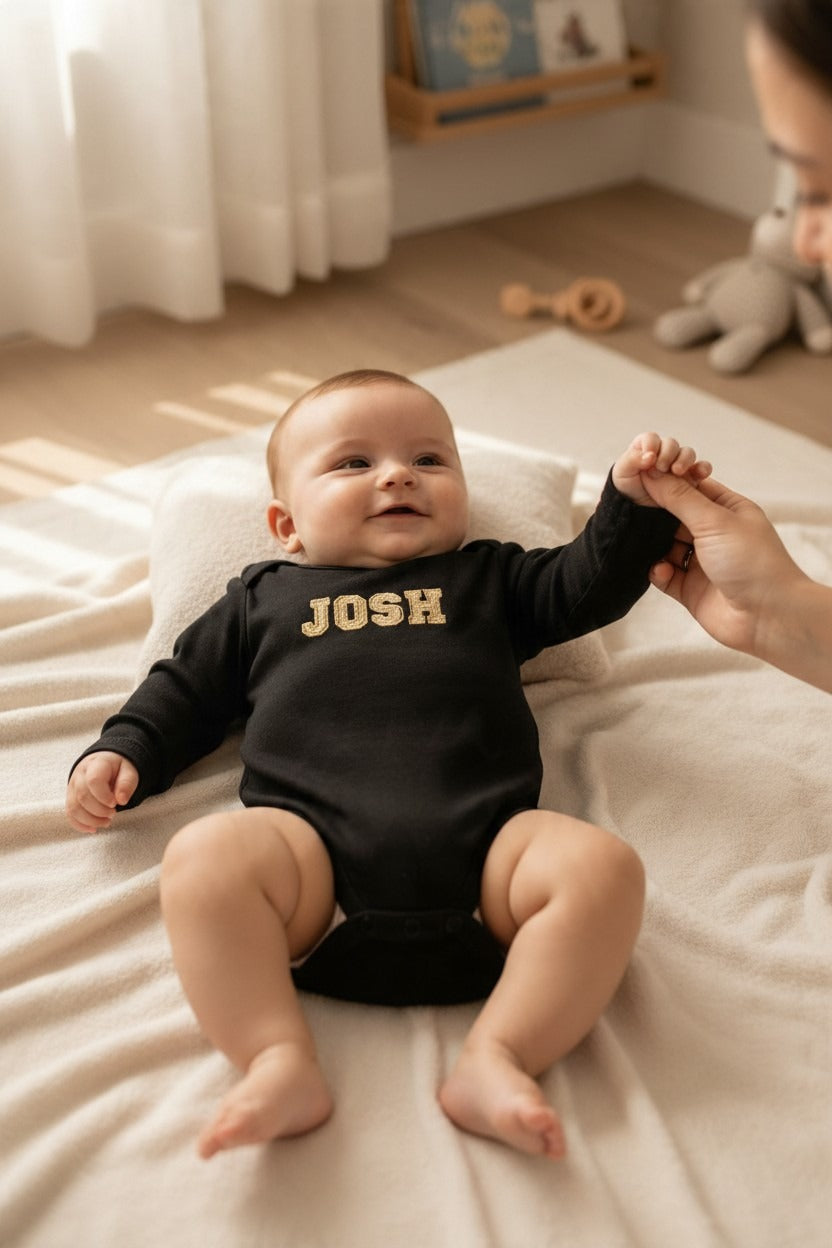 Baby in a black long sleeve suit with the name JOSH embroidered in gold