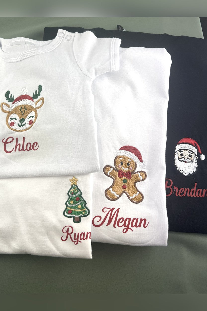 Folded embroidered Christmas tees and baby suit with Santa, gingerbread, tree and reindeer logos and printed names