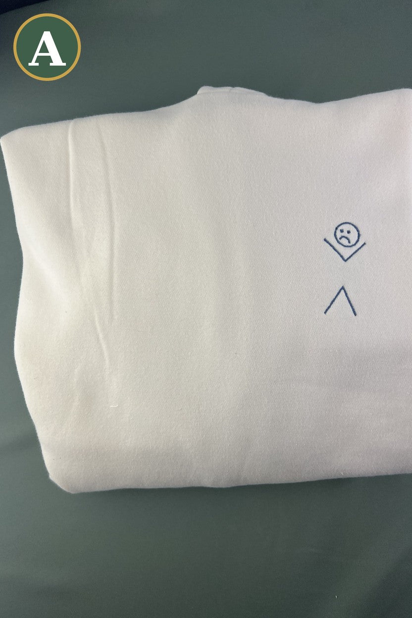 Folded ivory hoodie with a small embroidered sad stick figure on the chest, option A